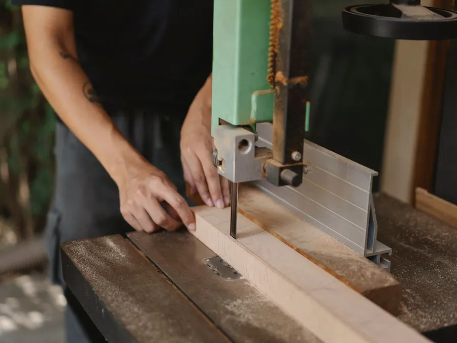 Faceless carpenter cutting timber with band saw on table