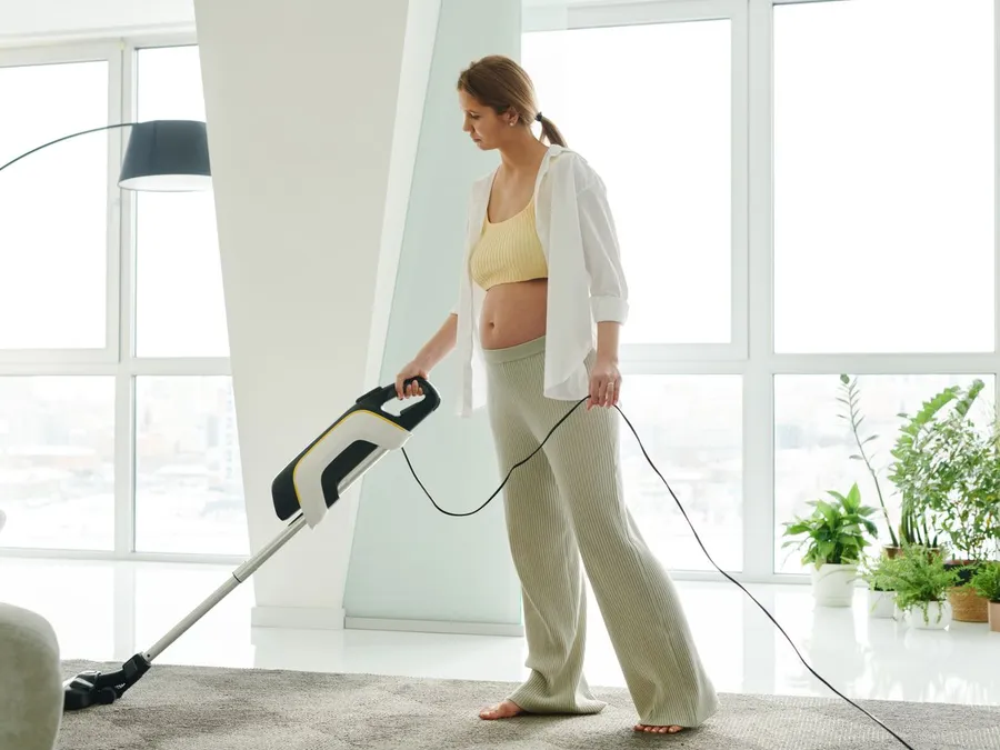 A Woman Using a Vacuum while Cleaning the Carpet