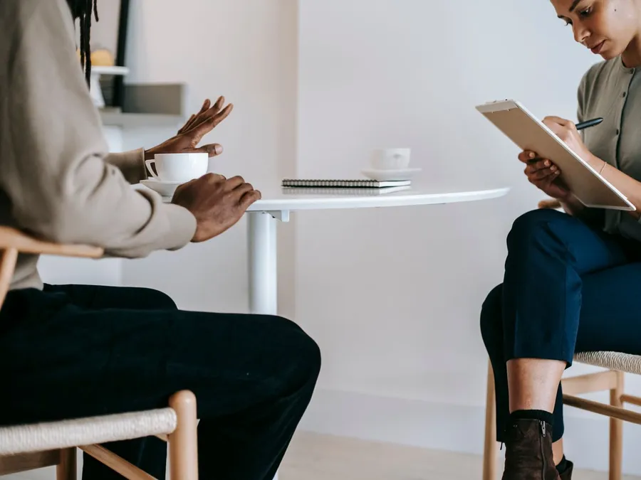 Crop ethnic female consultant talking to client and taking notes