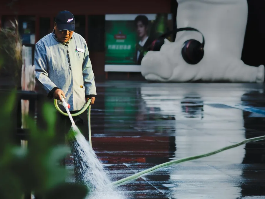 Street Cleaner Washing Pavement Near Sculpture